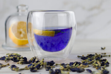 Glass cup of organic blue Anchan tea on a light foil, close-up. Herbal tea. Clitoria ternatea