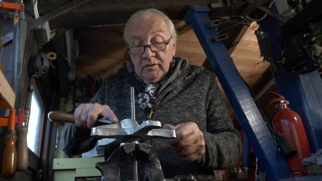 Senior male mechanic using file to work on a machine part in old workshop