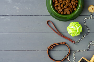 Bowl with dry pet food and toys on gray wooden background