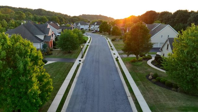 Upscale USA neighborhood during summer sunset. Aerial flight over street with large mansions in suburb.