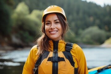 Portrait of smiling young woman in yellow life jacket and helmet standing on kayak.
