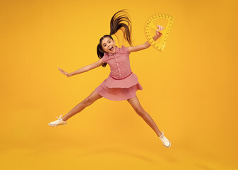 Amazed teenager. Measuring school equipment. Schoolgirl holding measure for geometry lesson, isolated on yellow background. Crazy jump, jumping kids. Student study math. Excited teen girl.