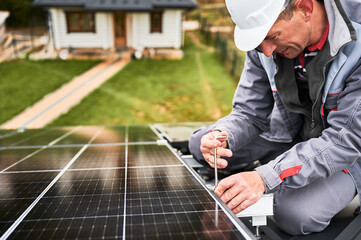 Man engineer mounting photovoltaic solar panels on roof of house. Technician in helmet installing solar module system with help of hex key. Concept of alternative, renewable energy.