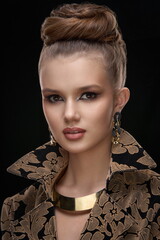 Portrait of a young girl with exquisite makeup and a high stylish hairstyle with gold jewelry on her neck