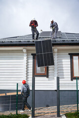 Men workers installing solar panel system on roof of house. Electricians in helmets lifting up...