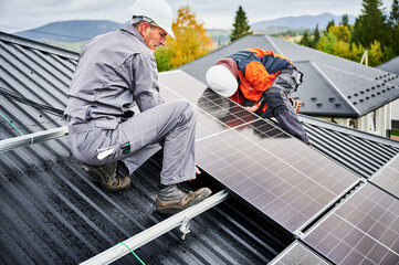 Electricians building photovoltaic solar module station on roof of house. Men technicians in...