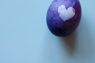 purple egg with heart dyed blueberries for easter on blue background with copy space