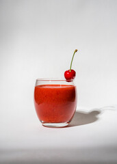 Glass with strawberry, red smoothie and on a white background. There's a cherry on the glass. Summer drink. Vitamins, diet, proper nutrition, veganism
