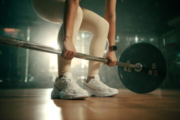 Young woman doing deadlift with heavy bar in gym, strong female athlete with muscular body lifting weights, exercising with barbell.