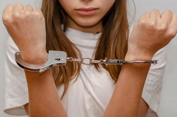 Teenage girl in handcuffs on gray background. Juvenile delinquent, criminal responsibility of...