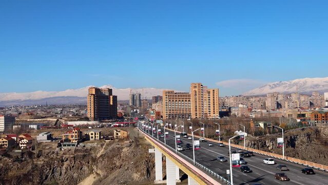 Camera moves from left to right, capturing the movement of cars on Davtashen Bridge over Hrazdan Gorge on a clear sunny winter day, set against the backdrop of snow-covered Aragats and Ara mountains