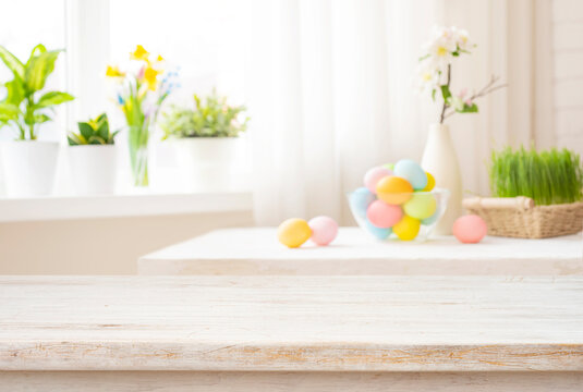 Easter table with colorful eggs and spring flowers on blurred kitchen window background