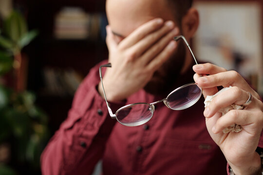 Selective focus closeup of unrecognizable bearded man taking off eyeglasses to rub his eyes during therapy session