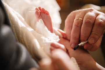Unction at baptism. Closeup of tiny baby feet, the sacrament of baptism ceremony. Godmother holds...