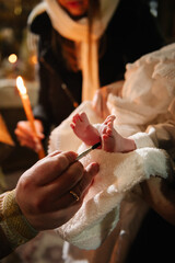 Unction at baptism. Closeup of tiny baby feet, the sacrament of baptism ceremony. Godmother holds...