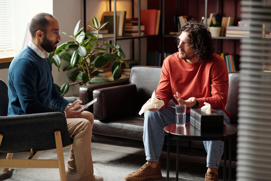 Despaired young man telling professional psychologist about his problems during therapy session