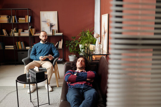High angle view wide shot of young Middle Eastern psychologist conducting therapy session of Caucasian man with depressive disorder