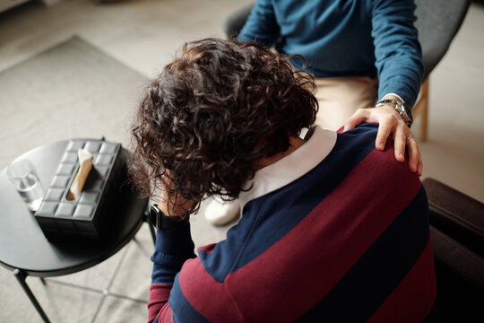 High angle view of unrecognizable psychologist comforting depressed man with messy curly hair giving him supportive touch