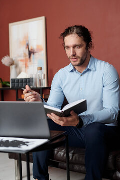 Vertical medium long portrait of psychologist holding notebook sitting in front of laptop working with patient through video call