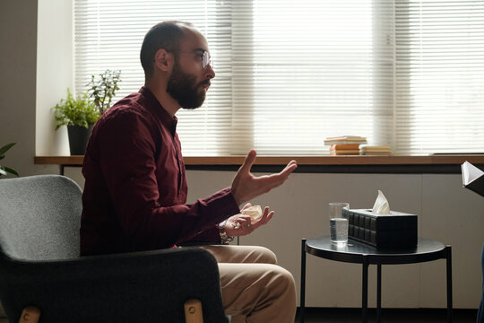 Side view of Middle Eastern man sitting on chair speaking about his troubles at therapy session
