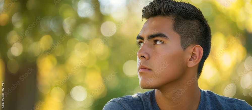 Wall mural Serious young Hispanic man in park, looking to the side.