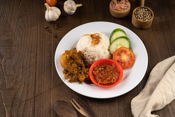 Ayam Goreng Lengkuas Kremes or Crispy Galangal Fried Chicken with steamed rice and chili paste or sambal on white plate and wood table