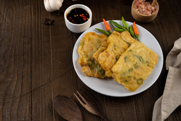 Deep fried tempeh or Tempe mendoan goreng made from soy bean with flour batter and spring onion on white plate. street food