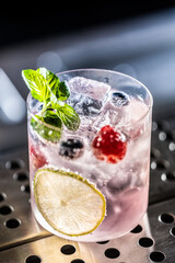 Pink cocktail Gin Tonic drink with raspberries, blueberries, lime and fresh mint