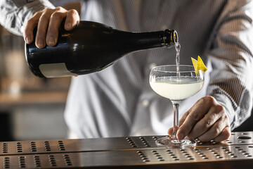 A bartender pours champagne or prosecco into a French 75 cocktail drink
