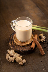 Hot ginger or wedang susu jahe milk with brown sugar, cinnamon, lemongrass and spice clove on wooden table.