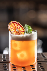 Glass of Jungle Bird cocktail garnished with dried red orange and mint leave on bar counter