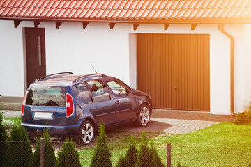 A blue family car sits peacefully in the driveway of a beautiful detached house with a brown garage...