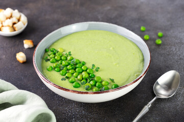Green pea cream soup with croutons on a brown table