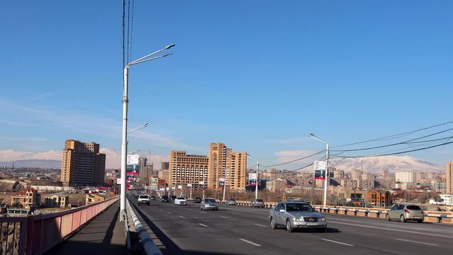 Cars traverse Davtashen Bridge over Hrazdan Gorge on a clear sunny winter day, set against the backdrop of snow-covered Aragats and Ara mountains, captured with handheld camera, uhd, 4k, 3840, 2160