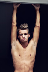 Fototapeta na wymiar Shirtless, body and portrait of young man looking serious on a dark background with strength. Topless, muscles and face of a caucasian male person from Norway with confidence and pride for his chest