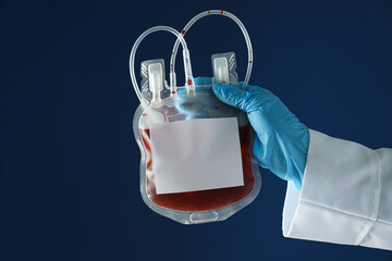 Bag with donor blood in gloved hand on blue background