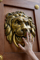 An old wooden door decorated with a lion's head as a knocker. Hand holding a door knocker. Knocking...