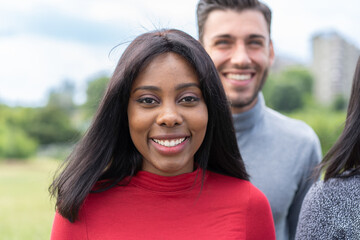 Fototapeta premium Vibrant portrait of a smiling young woman with diverse friends in a park, showcasing joy and multicultural relationships.