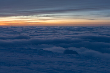 Sunset high in the mountains in winter. White clouds merge with snow to create a soft landscape. A...