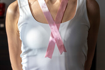 Shot of the woman in the white top against the white wall, with pink ribbon on her neck as a symbol...