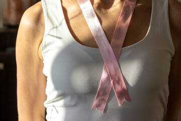 Shot of the woman in the white top against the white wall, with pink ribbon on her neck as a symbol of breast cancer awareness. Concept