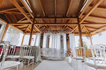 The white arch is decorated with pink flowers. White carpet and white chairs. Preparation for the wedding ceremony