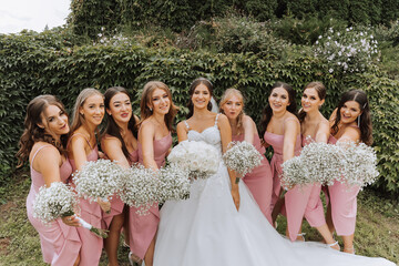 A brunette bride and her bridesmaids in matching pink dresses are standing with bouquets of flowers...