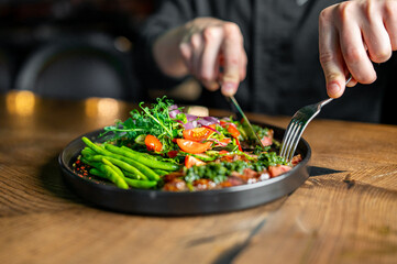 Hands of a man with a fork and knife eat Salad