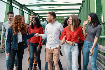 A group of multicultural friends walk relaxed and smiling on a city bridge, enjoying a day together.