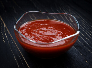 Ketchup in a glass cup on a black background.