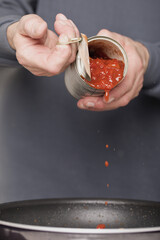 Older man in kitchen opening can of tomato sauce for spaghetti