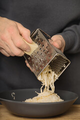 Older man in kitchen grating cheese for spaghetti with minced meat, tomatoes and gouda