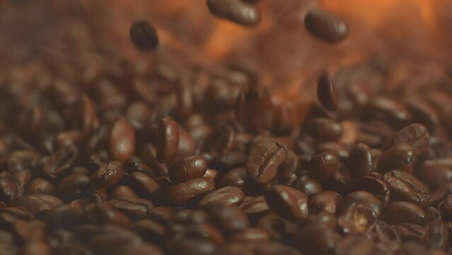 Super slow motion shot of falling hot roasted coffee beans with smoke in macro. Roasting and burning flying whole coffee with fire. Close up video