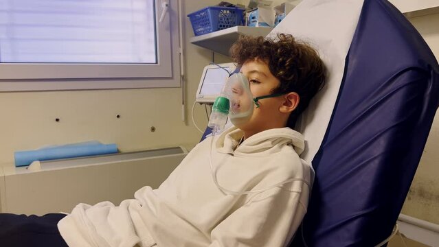 Sick teenager with an inhaler at hospital. An unhealthy child makes inhalations at hospital. Teenager to breath wears an oxygen mask to ease the course of the disease
